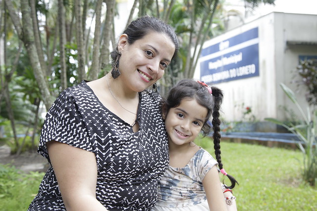 Paciente beneficiada pelo mutirão de otoplastia posando com a mãe em frente ao Hospital Municipal Nossa Senhora do Loreto