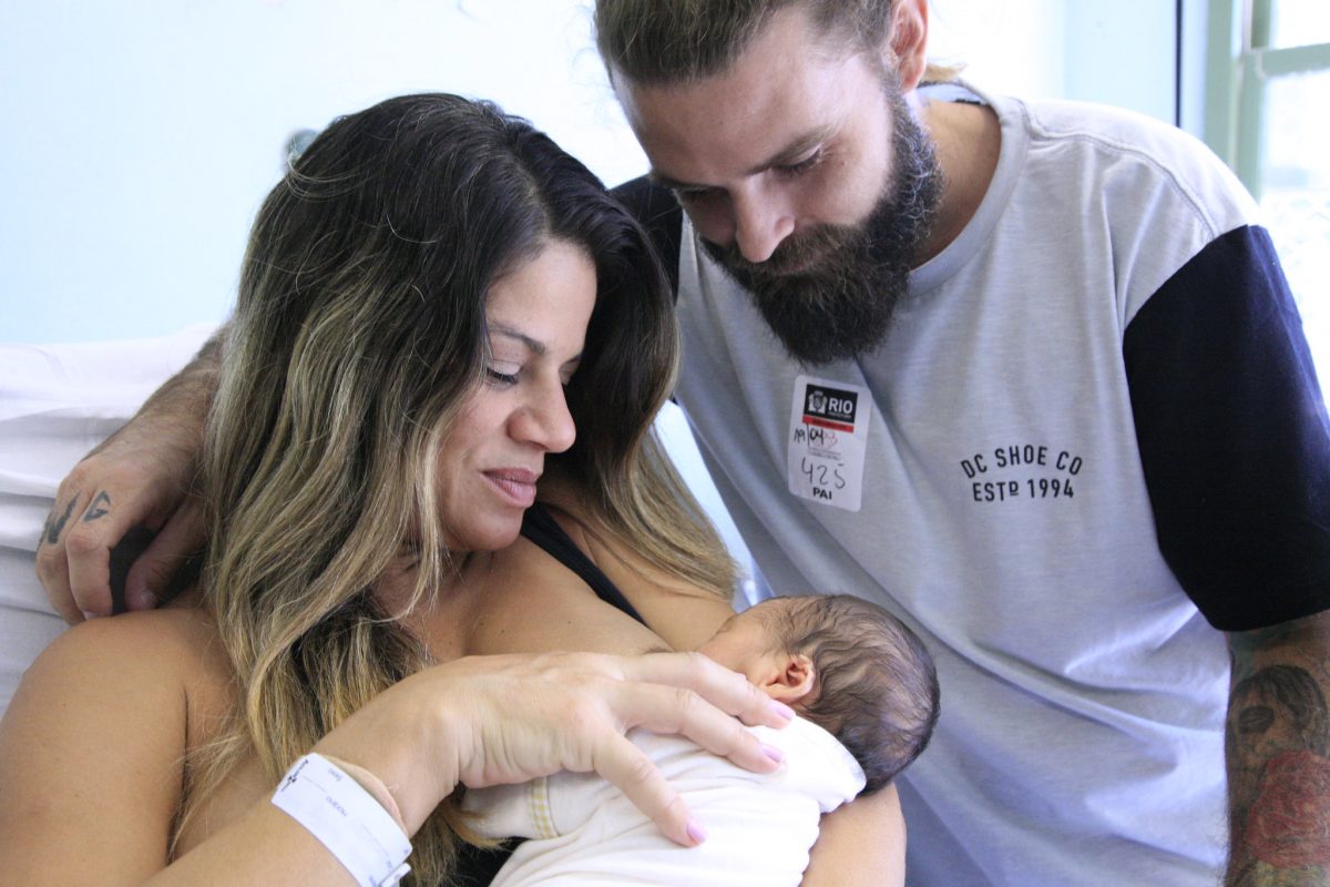 Mãe amamentando o filho e pai observa o bebê no colo da mãe