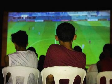 Garotos diante de telão com partida de futebol no videogame. Foto: divulgação