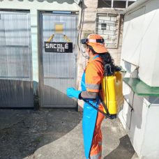 Funcionária da Comlurb higieniza porta de comércio em comunidade. Foto: divulgação / Comlurb